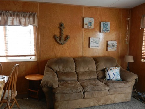 Cozy living room with a brown couch, wooden walls, nautical decor, and a small dining area with wooden chairs.
