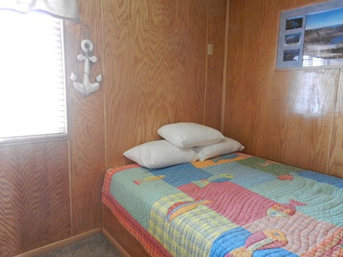 Cozy bedroom with a wooden wall, a bed covered in a colorful fish-patterned quilt, and two pillows.
