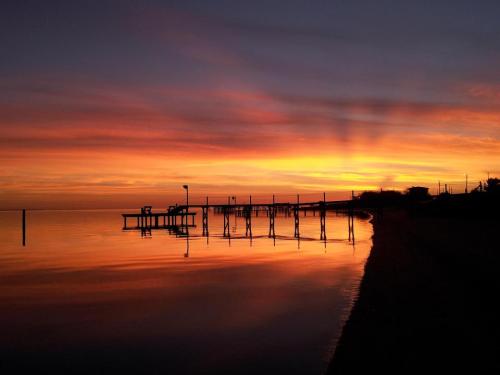 A serene sunset over calm waters, with a silhouetted pier and colorful sky reflecting on the surface.