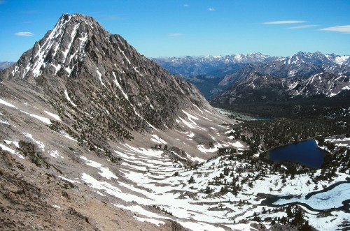 A panoramic view of a rugged mountain landscape with snow-capped peaks and a serene lake below.