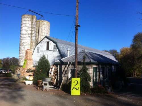 A rustic building with silos, surrounded by trees and outdoor decor, under a clear blue sky. A large yellow number 2 is visible.