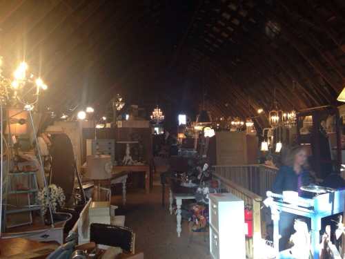 A spacious, dimly lit antique shop filled with various furniture and decorative items, featuring chandeliers and a wooden ceiling.