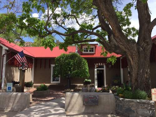 A charming building with a red roof, surrounded by greenery and an American flag, under a large tree.