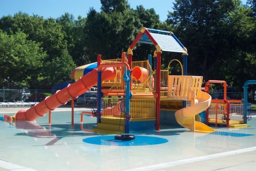 Colorful water play structure with slides and splash features in a sunny outdoor pool area.