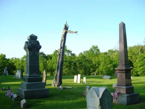 A serene cemetery scene with gravestones, a tall wooden structure, and small American flags on the grass.