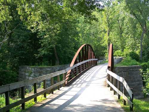 A curved metal bridge over a path surrounded by lush green trees and foliage.