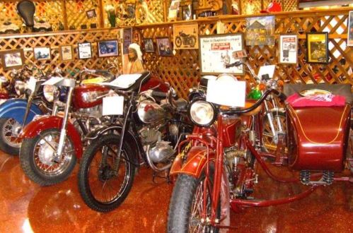 A collection of vintage motorcycles and a sidecar displayed in a rustic setting with wooden decor and memorabilia.