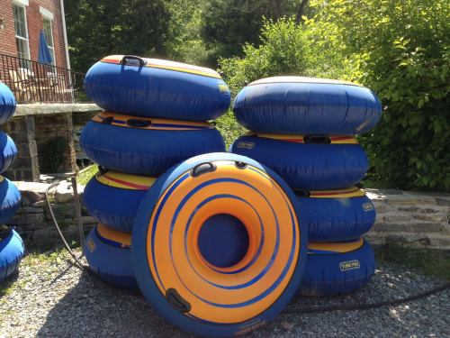 A stack of colorful inflatable tubes in blue and orange, resting on gravel near greenery and a building.