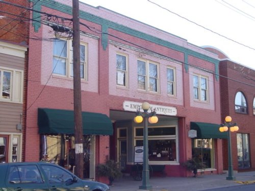 A pink brick building with green accents, featuring large windows and an antique shop sign, surrounded by street lamps.