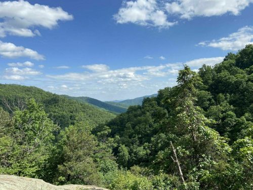 Lush green mountains under a blue sky with fluffy clouds, showcasing a serene natural landscape.