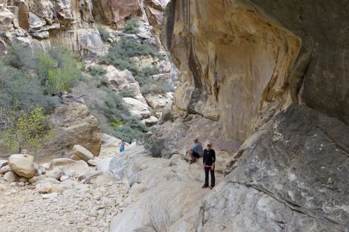 Hikers explore a rocky canyon with towering cliffs and sparse vegetation in a natural landscape.