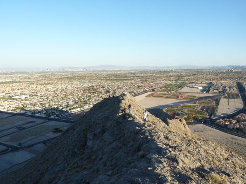 A panoramic view from a mountain peak overlooking a sprawling city and landscape under a clear blue sky.