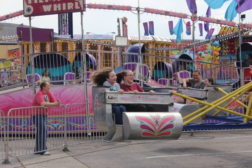 A group of people enjoy a spinning carnival ride, with colorful decorations and excited expressions.