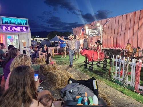 A lively outdoor event at night with people enjoying activities, hay bales, and a cowboy-themed setup.