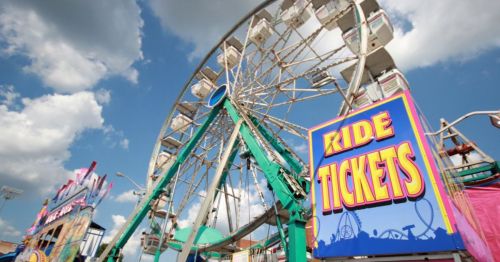 A colorful ferris wheel at a fair, with a sign reading "Ride Tickets" in the foreground against a blue sky.