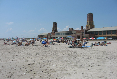 Crowded beach scene with people sunbathing and colorful umbrellas, featuring a large building in the background.