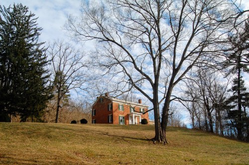 A brick house on a grassy hill, surrounded by bare trees under a cloudy sky.