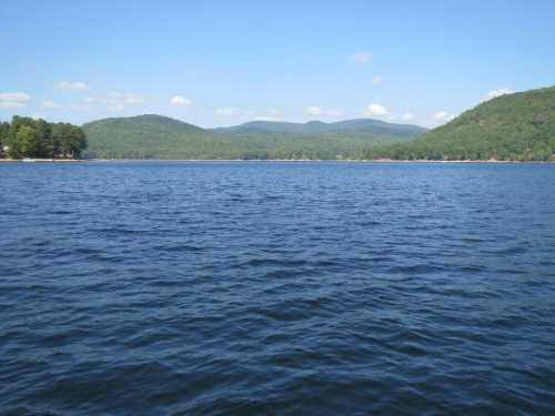 A serene lake surrounded by green hills under a clear blue sky, with gentle ripples on the water's surface.