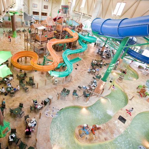 A vibrant indoor water park featuring slides, pools, and play structures, with guests enjoying the attractions.