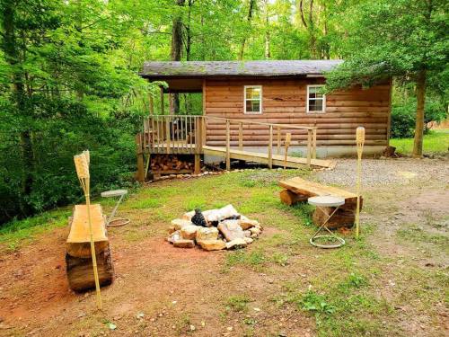 A cozy log cabin surrounded by trees, with a fire pit and wooden benches in a serene outdoor setting.