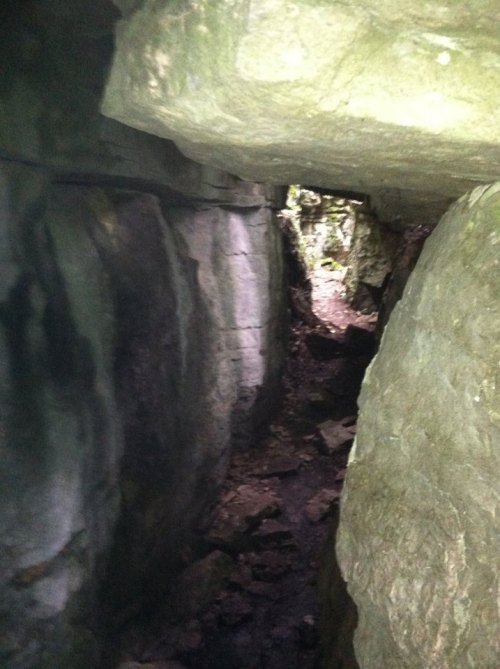 Narrow passage between large rocks in a cave, with uneven ground and dim lighting.