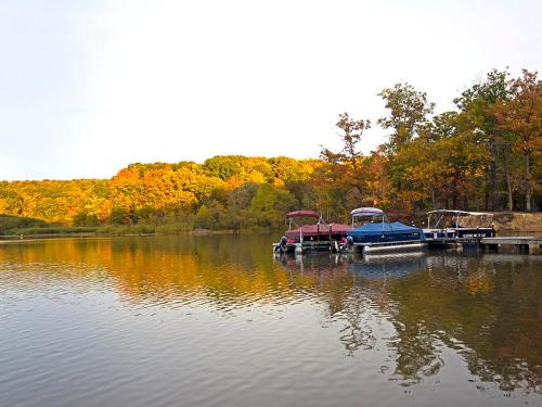 A serene lake scene with colorful autumn trees reflecting on the water, featuring boats docked at a pier.