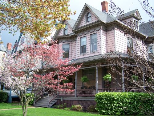 A charming Victorian house with a pink exterior, surrounded by blooming trees and lush green grass.