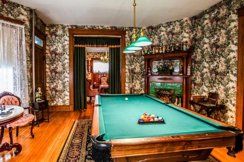 A vintage game room with a green pool table, floral wallpaper, and elegant furniture in a cozy setting.