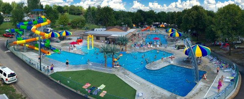 Aerial view of a vibrant water park with pools, slides, and colorful umbrellas, filled with people enjoying the sun.