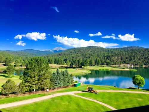 A serene landscape featuring a lake, green fields, trees, and mountains under a bright blue sky with fluffy clouds.