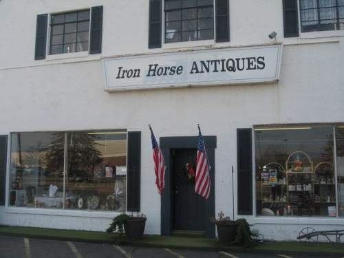 Exterior of an antique shop named "Iron Horse Antiques," featuring large windows and American flags at the entrance.