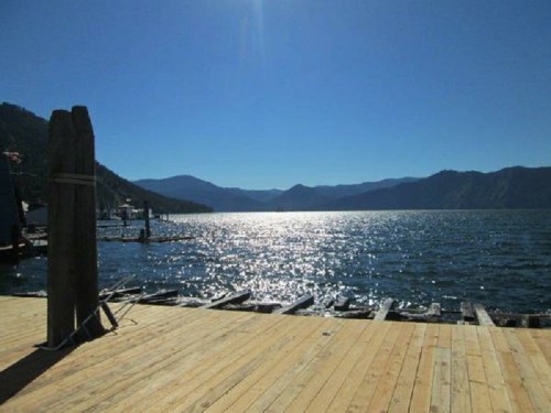 A serene lake view with mountains in the background, sunlight reflecting on the water, and a wooden dock in the foreground.