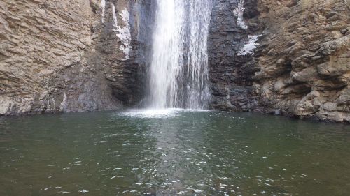 A serene waterfall cascading into a calm pool surrounded by rocky cliffs.