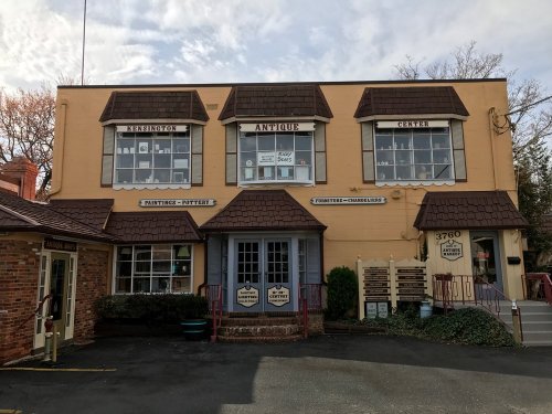 A two-story building with a sloped roof, featuring antique shops and large windows, set against a cloudy sky.