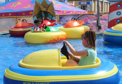 Two children in colorful bumper boats on a sunny day, enjoying a water attraction at a fair.