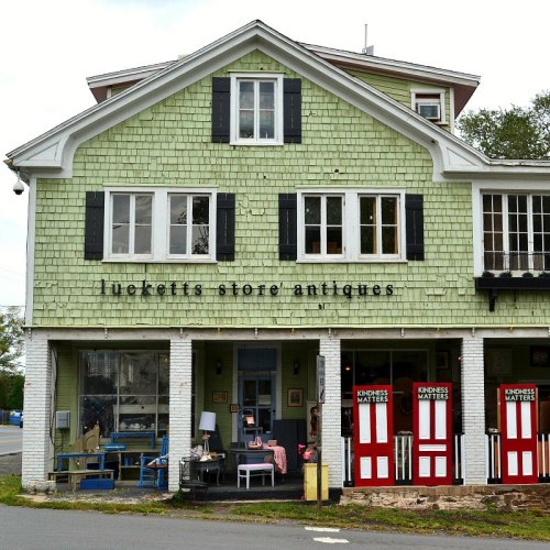 A green antique store with black shutters and a sign reading "Luckett's Store Antiques," featuring a welcoming entrance.
