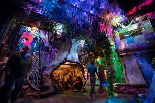 A vibrant, whimsical indoor space with colorful lights, tree-like structures, and people exploring the enchanting environment.