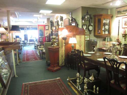 A vintage shop interior filled with antique furniture, lamps, and decor, featuring a dining table and rugs.