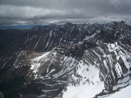 A panoramic view of rugged, snow-capped mountains under a cloudy sky, showcasing dramatic peaks and valleys.