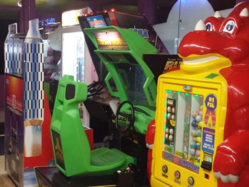 A colorful arcade with a green racing game and a red dragon-themed prize machine.