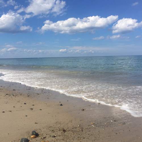 A serene beach scene with gentle waves lapping at the shore under a partly cloudy sky.