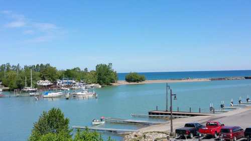 A serene waterfront scene with boats docked, lush greenery, and a clear blue sky over calm waters.