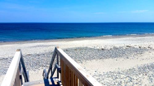 A wooden staircase leads down to a serene beach with clear blue water and a clear sky.