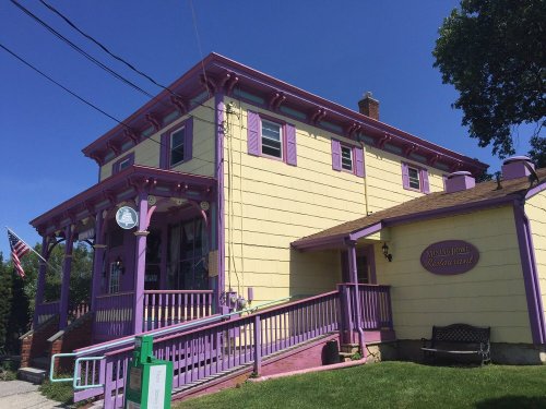 A yellow building with purple trim and accents, featuring a porch and a sign, set against a clear blue sky.