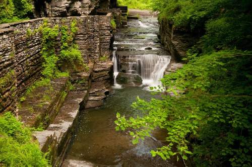 A serene waterfall cascades over rocky ledges, surrounded by lush green foliage and tranquil water.