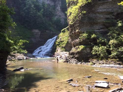 A serene waterfall cascades into a clear pool, surrounded by lush greenery and rocky cliffs.