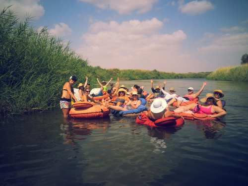 A group of people in inner tubes enjoying a sunny day on a river, surrounded by tall grass and blue skies.
