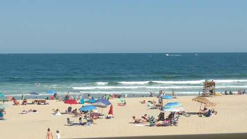 A sunny beach scene with people relaxing under colorful umbrellas by the ocean, waves gently lapping at the shore.