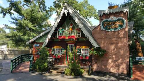 A whimsical, colorful cottage with a sloped roof, surrounded by greenery and decorated with flowers and a sign reading "Storybook Land."