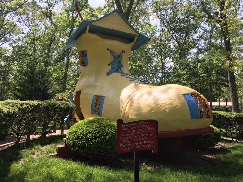 A large, whimsical yellow shoe-shaped structure surrounded by greenery, with a sign nearby explaining its significance.